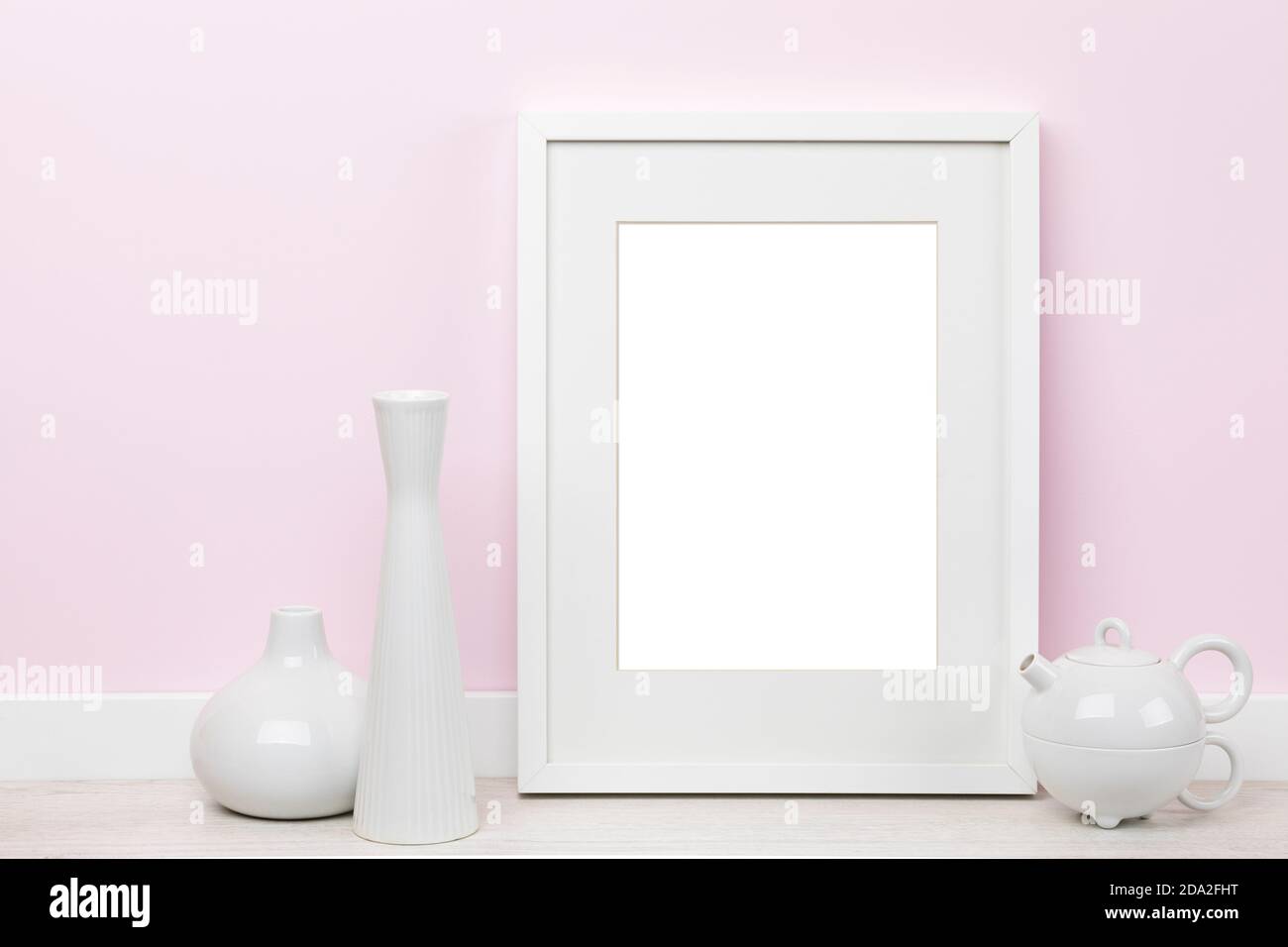 Elegantes Mockup mit weißem vertikalen Bilderrahmen mit matt, Vasen und Teekanne vor rosa Wand. Leerer Bildbereich mit Beschneidungspfad maskiert Stockfoto