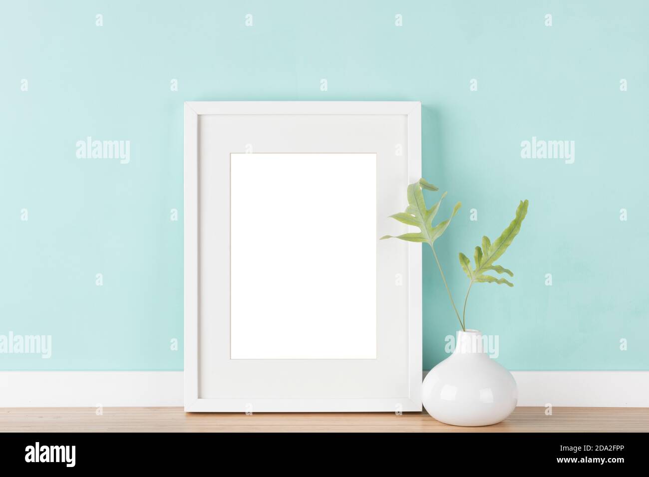 Elegantes Mockup mit weißem Bilderrahmen mit mattem, Vase mit Farnblättern vor pastellgrüner Wand. Leerer Bildbereich mit Beschneidungspfad maskiert Stockfoto