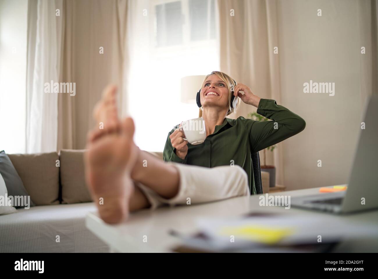 Porträt einer glücklichen Geschäftsfrau drinnen im Büro sitzen am Schreibtisch, halten Tasse Tee. Stockfoto
