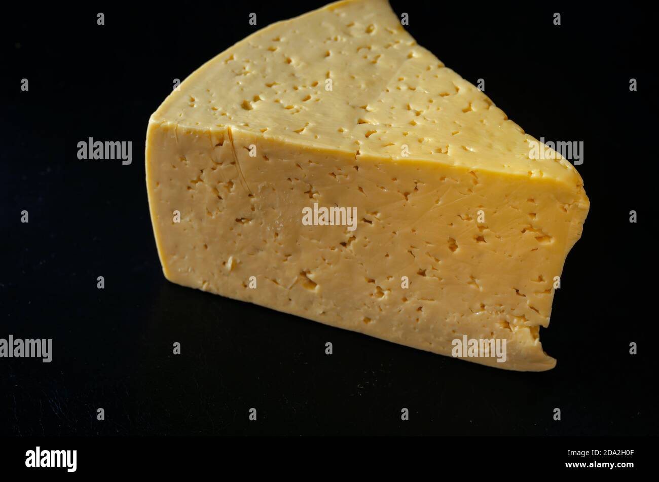 Stück Hartkäse auf schwarzem Hintergrund. Ein großes dreieckiges Stück echten Käses. Produkte, Zutaten. Stockfoto