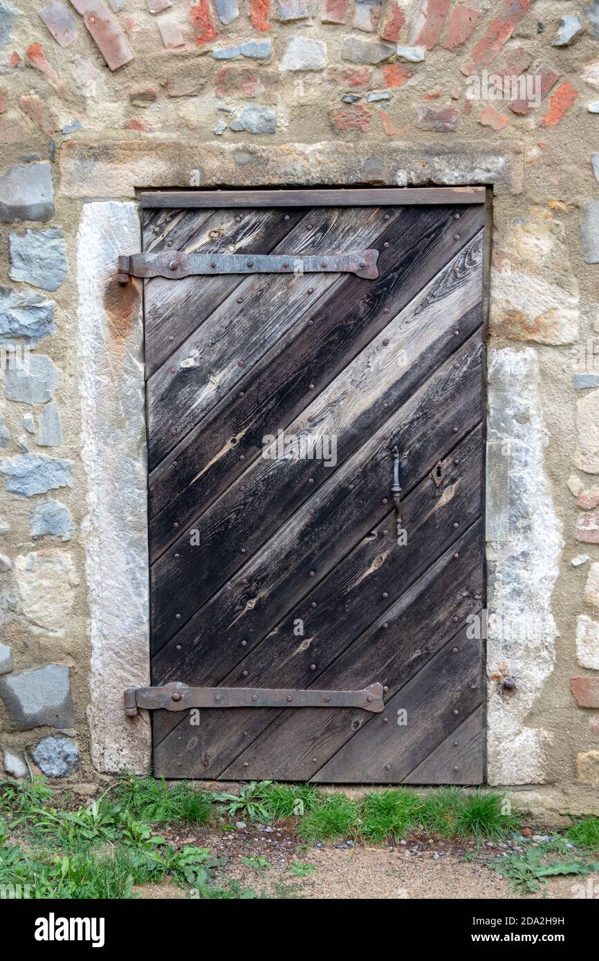 Vintage hölzerne Scheune Tür in einer Ruine der Burg eingezäunten Steinmauer mit Beton und Ziegel. Rustikale alte Türen. Stockfoto