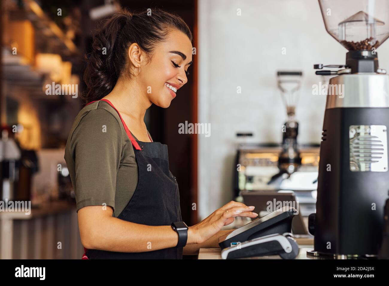 Seitenansicht der lächelnden Kellnerin im Vorfeld beim Eintippen von digitalem Bargeld Terminal im Café Stockfoto