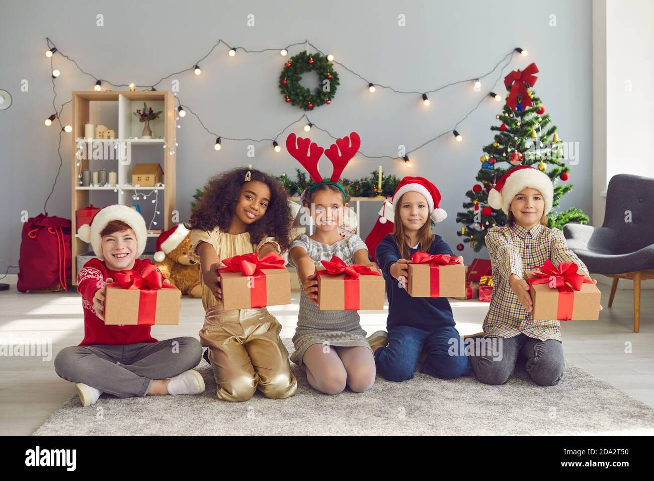 Kinder verschiedener Nationalitäten sitzen in einer Reihe und halten Weihnachtsgeschenke vor sich. Stockfoto