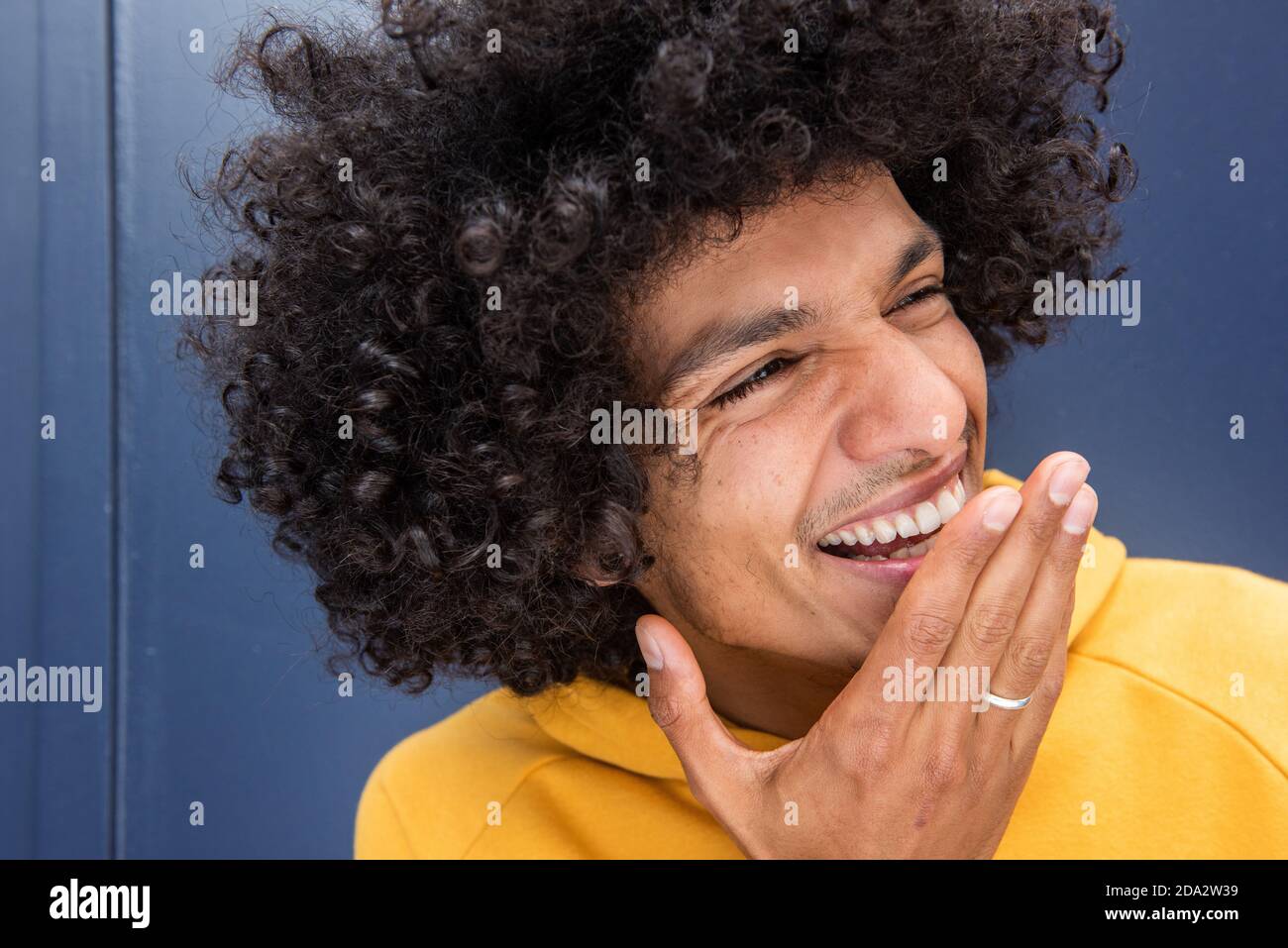 Portrait fröhlicher junger Mann lachend mit der Hand bedeckt Mund durch Blauer Hintergrund Stockfoto