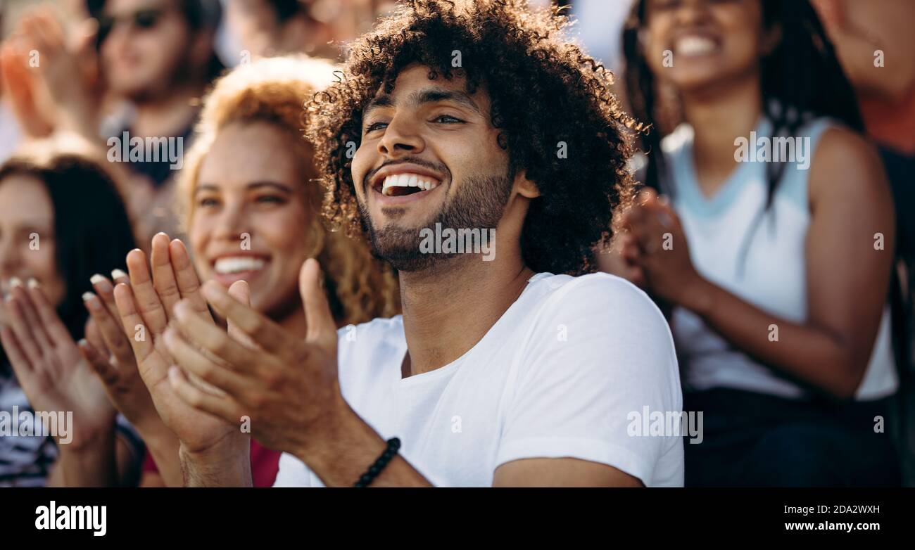 Lächelnder Mann, der ein Fußballspiel ansieht und im Stadion applaudiert. Begeisterte Sportfans applaudieren und feiern den Sieg ihrer Mannschaft. Stockfoto