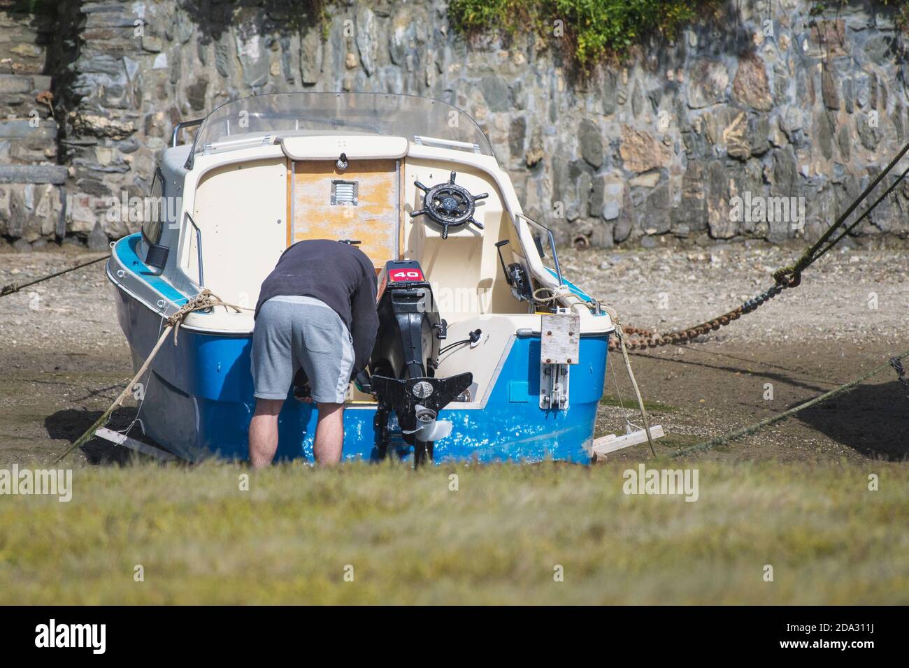 Ein Bootsbesitzer, der an seinem kleinen Motorboot arbeitet, legte bei Ebbe in Newquay in Cornwall am Gannel River fest. Stockfoto