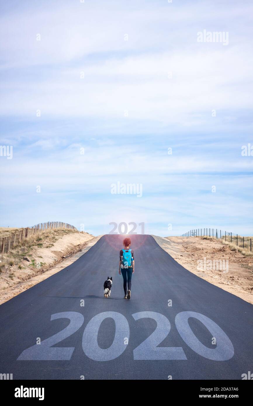 Beginnen Sie ein neues Jahr. Lassen Sie 2020 hinter sich. Lifestyle-Fotografie, Frau mit Hund auf der Straße auf der Suche nach Abenteuer Stockfoto