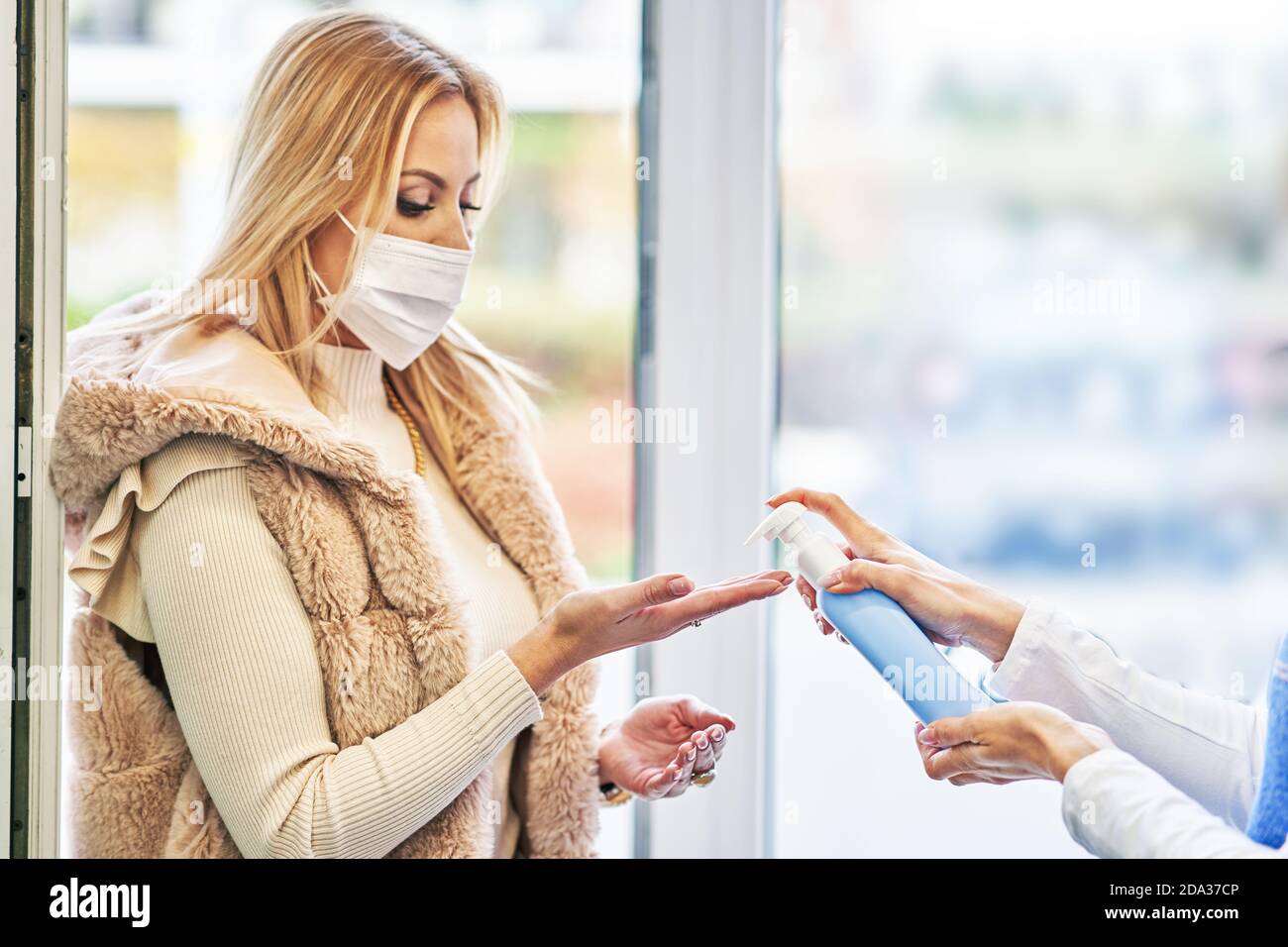 Erwachsene Frau in medizinische Maske mit Handdesinfektionsmittel vor dem Einkaufen Für Lebensmittel Stockfoto