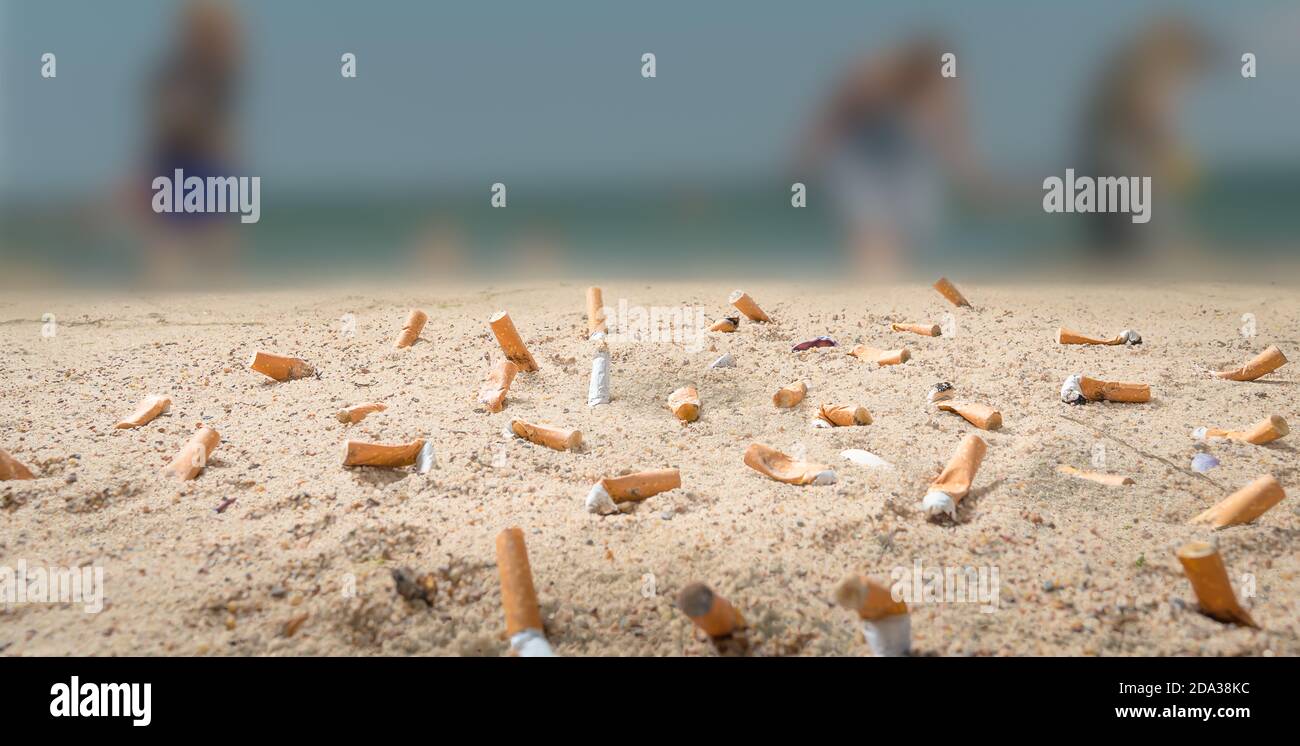 Viele Zigarettenkippen verschmutzen einen Strand, an dem nicht erkennbare Menschen hingehen Im Urlaub Stockfoto