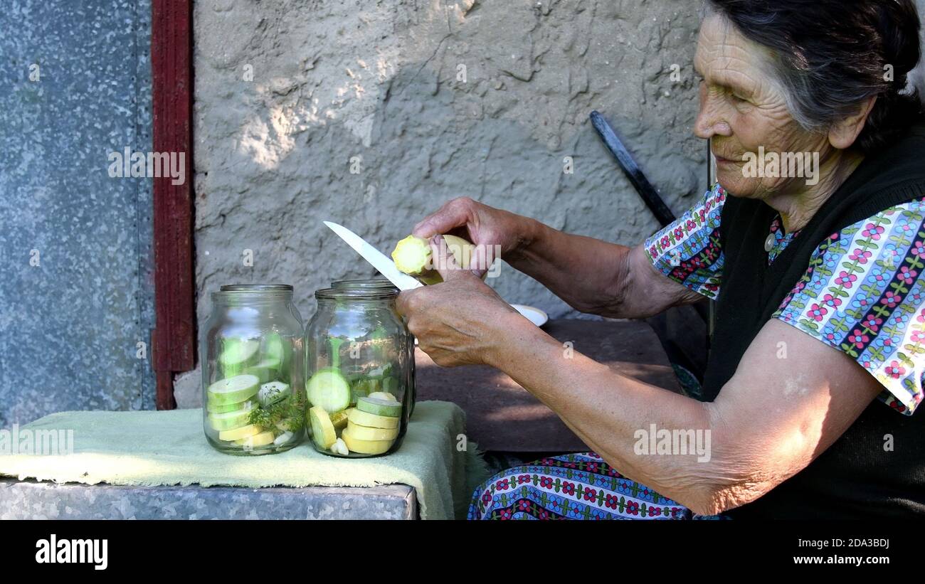 Faltige ältere Frau lächeln und schneiden rohen Kürbis und setzen Sie in ein Glas für hausgemachte Konservierung mit Dillsamen und Knoblauch. Ländliche lokale Küche mit Bio-ve Stockfoto