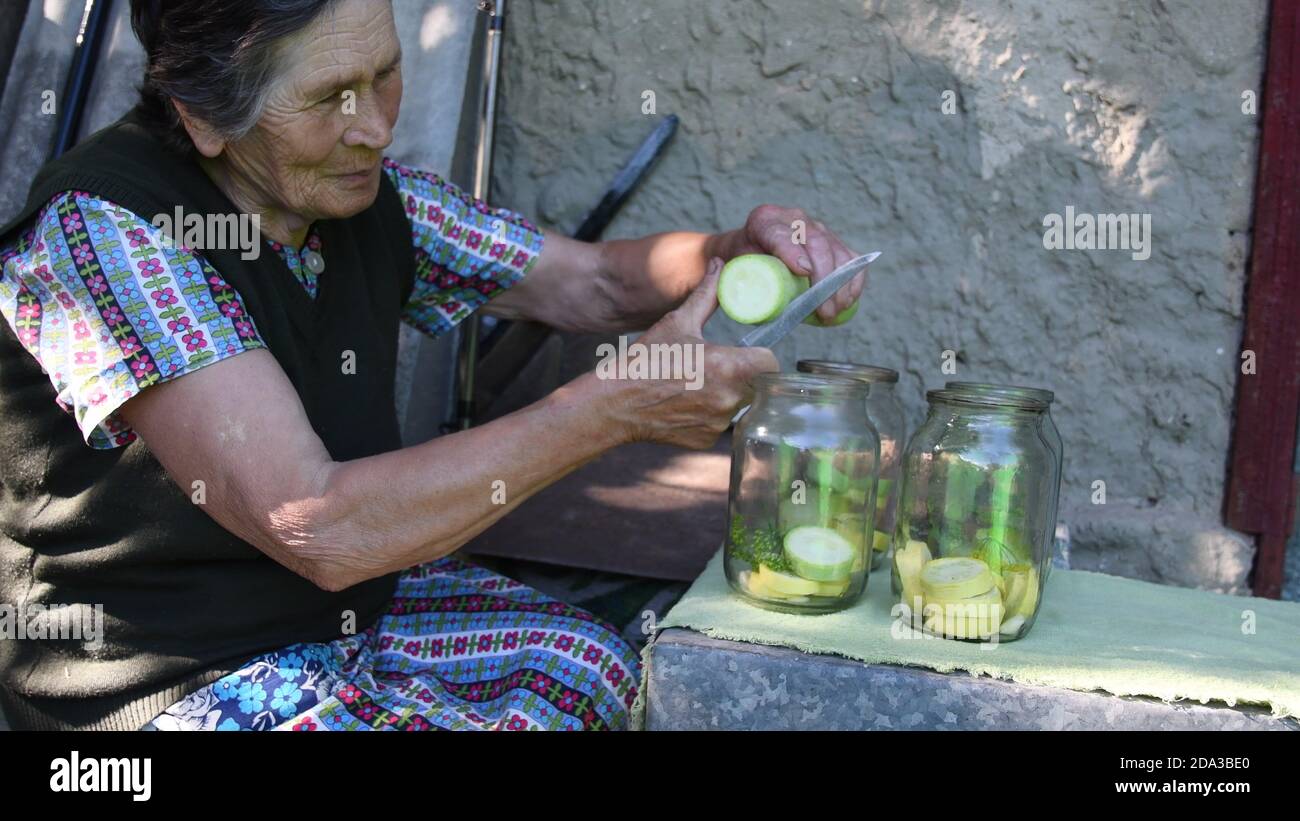 Senior asiatische Frau schneiden und schneiden frischen Squash und in Gläser für hausgemachte Konservierung. Oma bereiten Gemüse als Konservierung in Gläsern Stockfoto