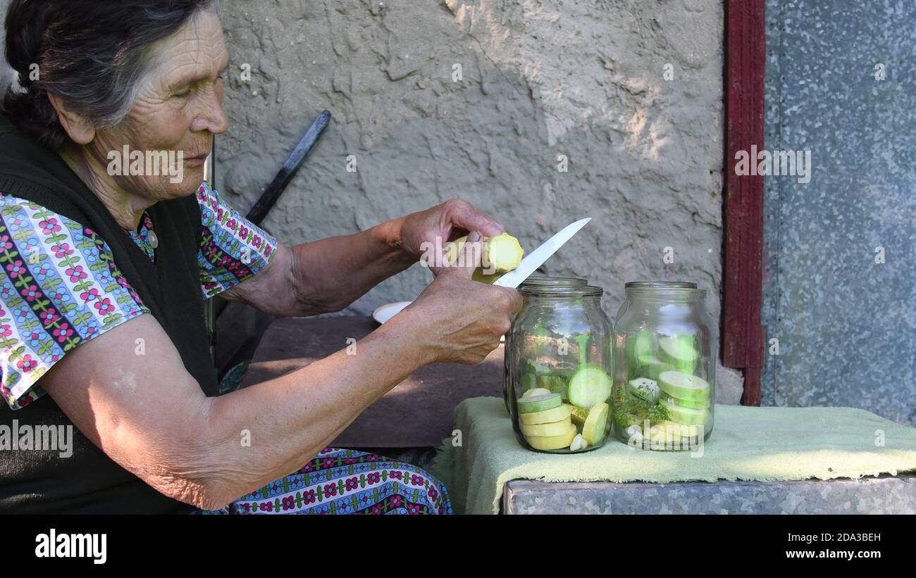 Faltige ältere Frau lächelt und sagt etwas über das Kochen dann schneiden rohen Kürbis und setzen in Glas für hausgemachte Einmachungen mit Dillsamen und Knoblauch. Stockfoto