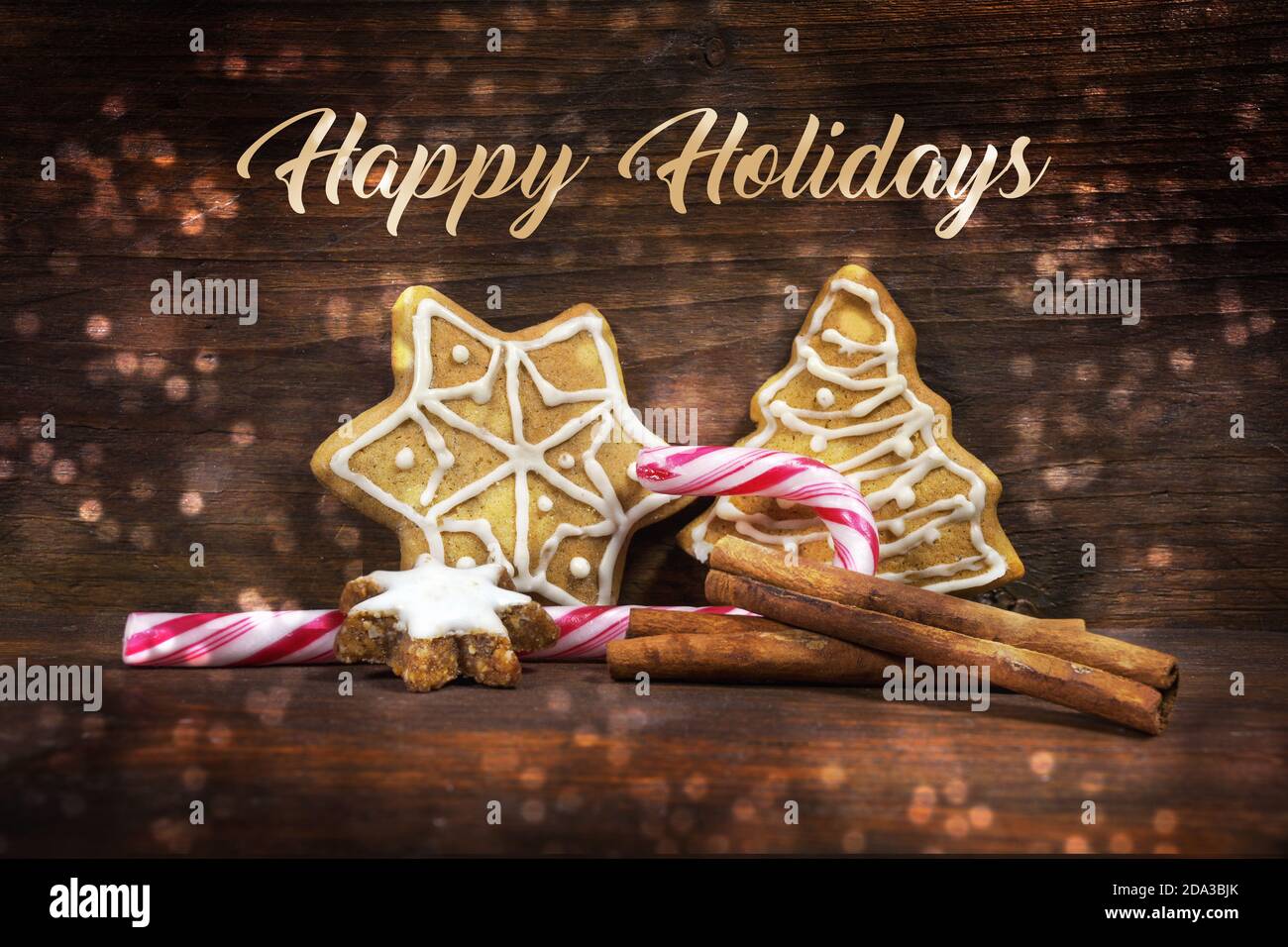 Lebkuchen, Zimtstern und Zuckerrohr, Süßigkeiten für Weihnachten und Advent, Text Happy Holidays, brauner Holzhintergrund mit Bokeh-Lichtfleck Stockfoto