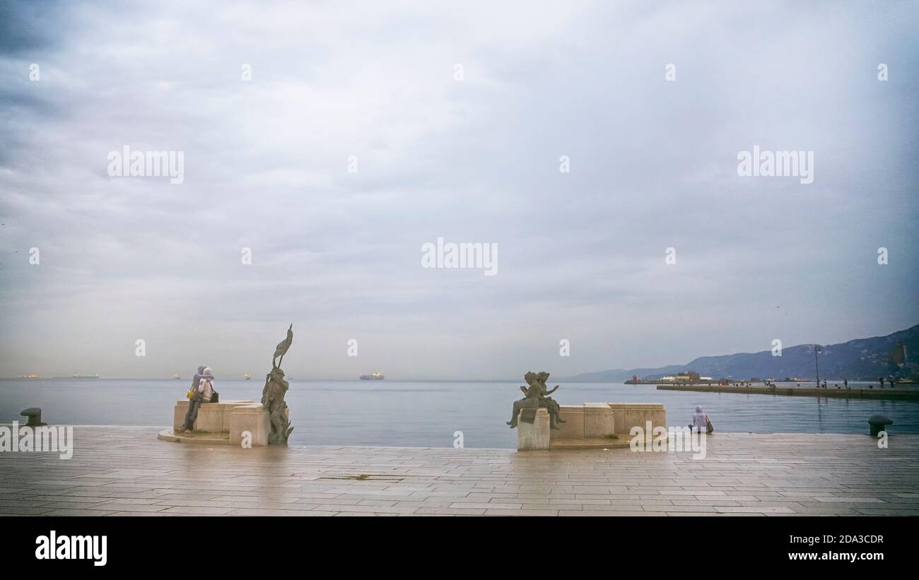 Triest, Italien. Piazza Unità. Ansicht der Bronzestatuen auf der Scala reale (Königliche Treppe). Auf der rechten Seite der Fampus Pier Molo Audace. Stockfoto