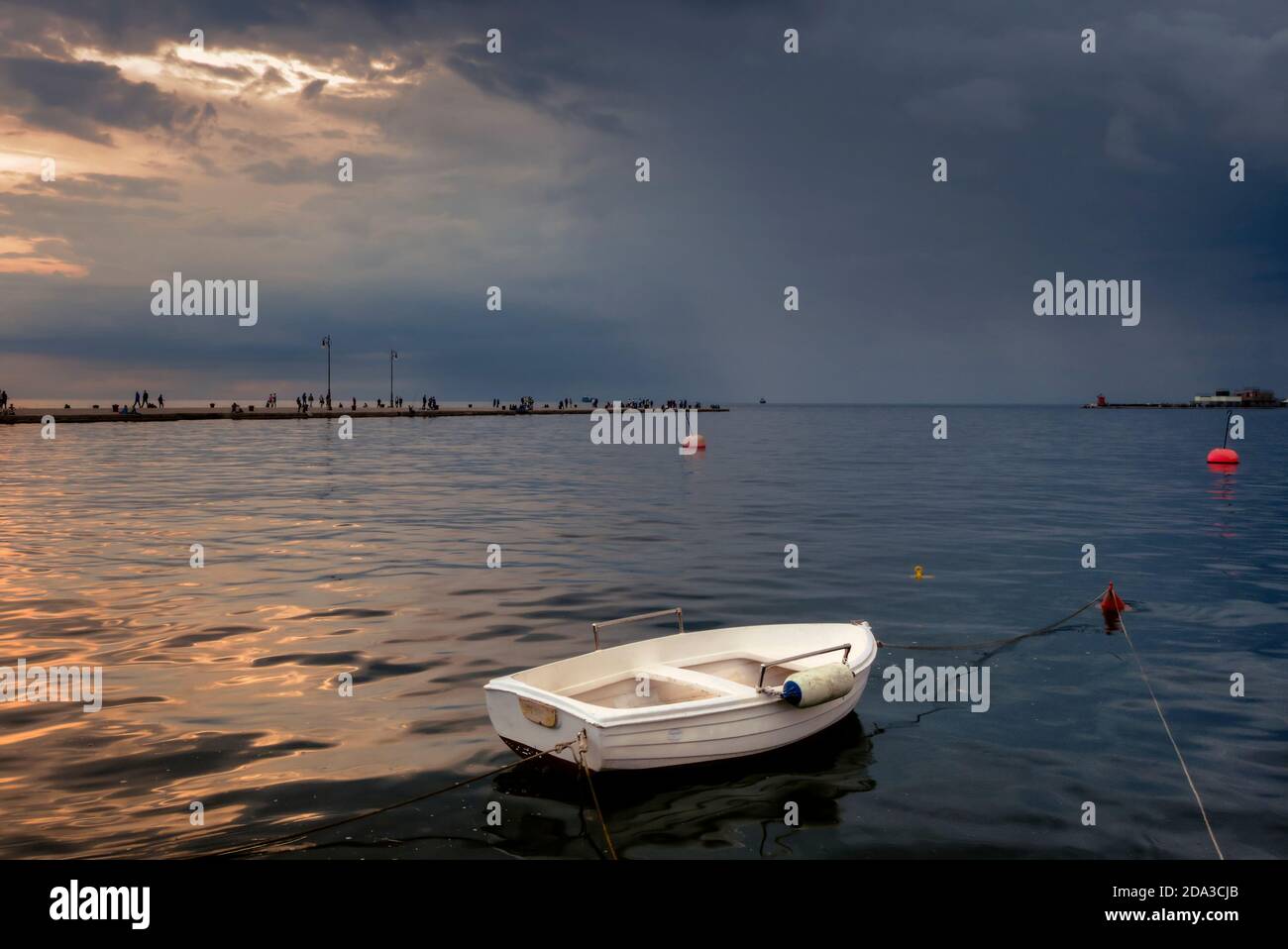 Triest, Italien. Ein weißes kleines Boot, das nahe am Rand verankert ist. Im Hintergrund der Pier Molo Audace. Stockfoto