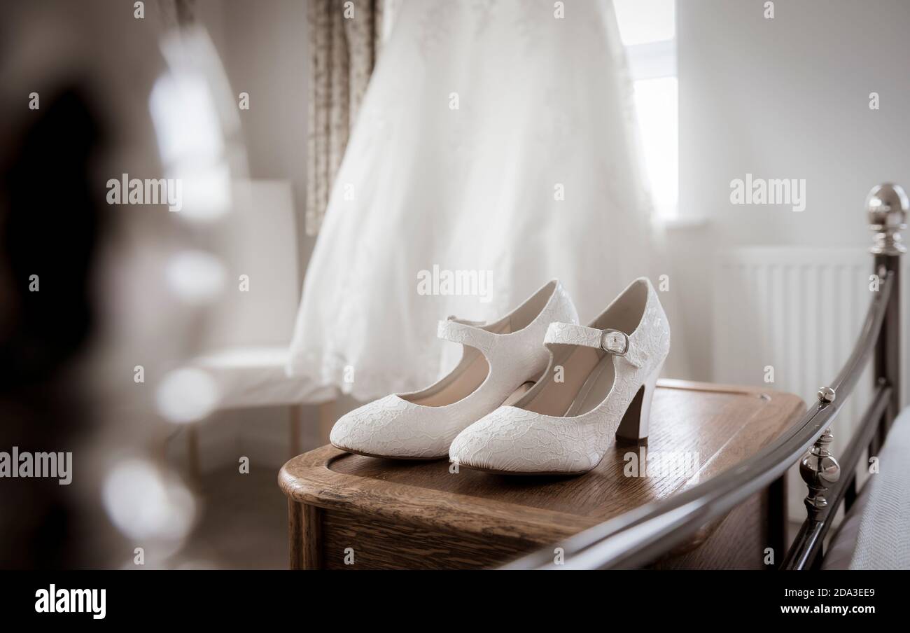 Brautkleid hängt an einem Schlafzimmerfenster mit Schuhen im Vordergrund. Stockfoto