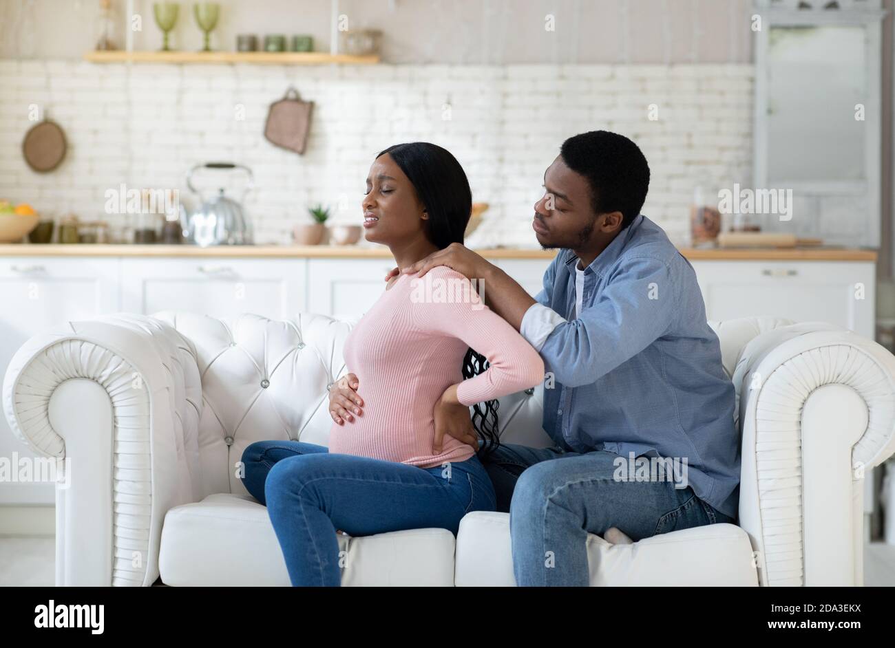 Schwarze schwangere Frau, die unter Rückenschmerzen leidet, liebevoller Ehemann, der zu Hause ihre Schultern massiert Stockfoto