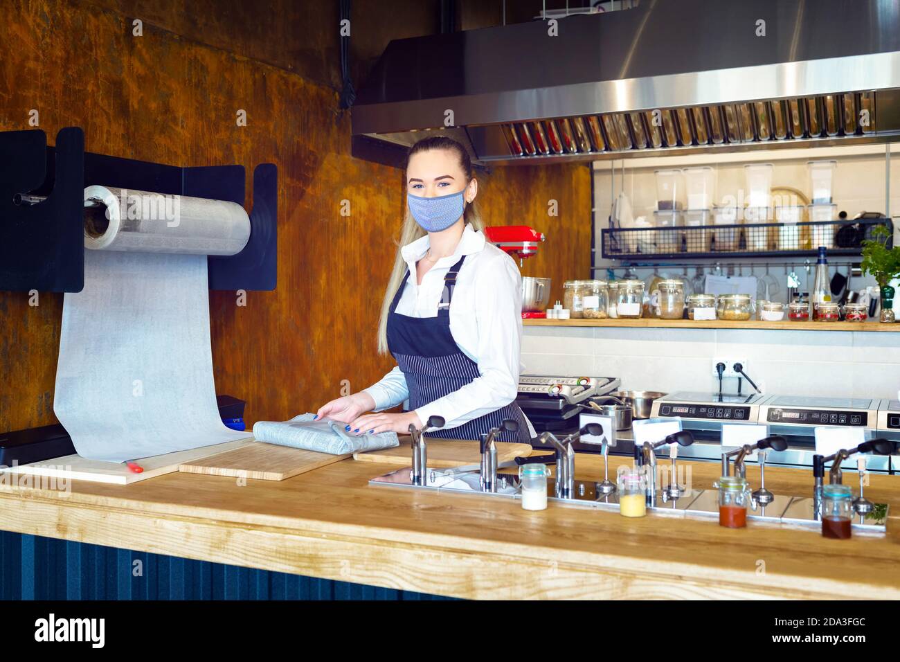 Glückliche Kellnerin trägt Gesichtsmaske Vorbereitung Essen zum Mitnehmen hinter dem Restaurant Zähler während der Coronavirus-Sperre Stockfoto