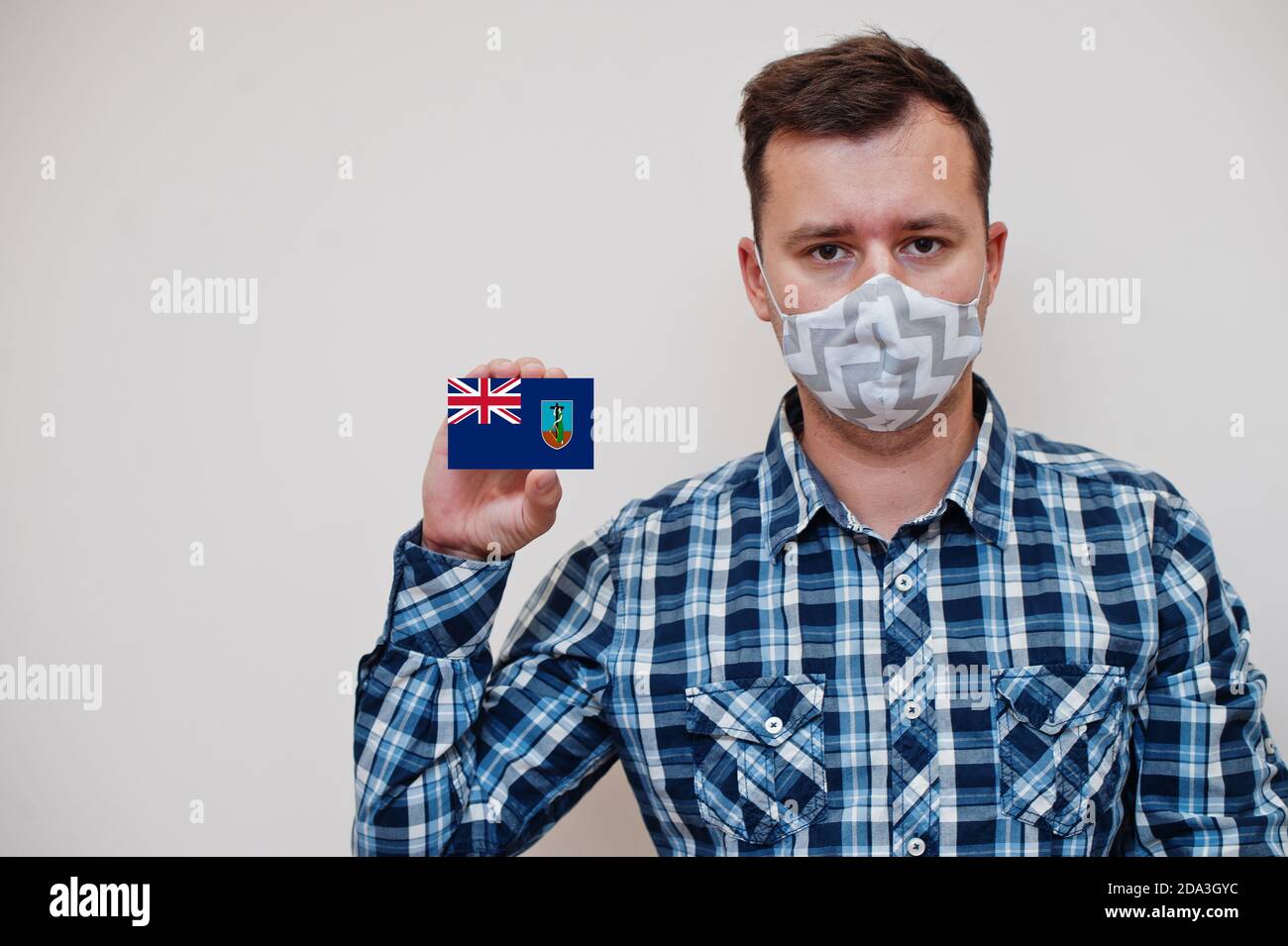 Mann im karierten Hemd zeigen Montserrat Flagge Karte in der Hand, tragen Schutzmaske isoliert auf weißem Hintergrund. Amerikanische Länder Coronavirus Konzept. Stockfoto