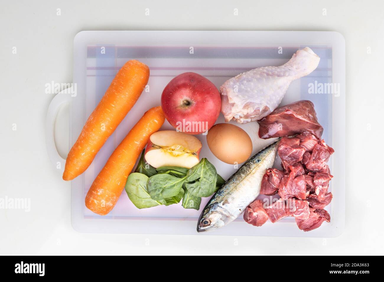 Overhead-Ansicht der Zutaten von Barf Rohkost Rezept für Hunde bestehend aus Fleisch, Organe, Fisch, Eier und Gemüse auf Schneidebrett Stockfoto
