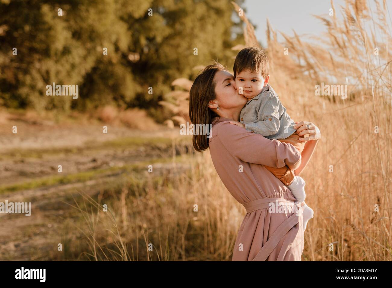 Portrait einer glücklichen, liebevollen Mutter, die ihren kleinen Sohn im sonnigen Park am Fluss umarmt. Stockfoto