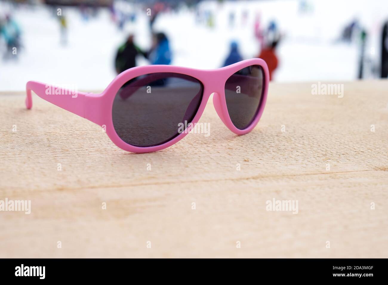 Rosafarbene Sonnenbrille auf einer Holzpiste in der après-Ski-Bar oder im Café, mit Skipiste im Hintergrund, Kopierraum. Konzept der Wintersport, Freizeit, recreati Stockfoto
