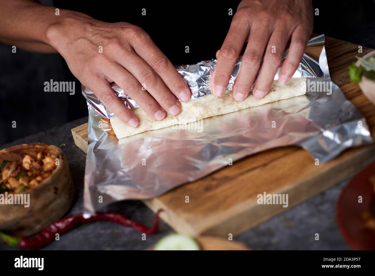 Nahaufnahme eines jungen Mannes, der in Aluminiumfolie ein Durum oder einen Burrito einwickelt, gefüllt mit Hühnerfleisch, das mit verschiedenen Gemüsesorten wie Zwiebeln oder Rot gekocht wird Stockfoto