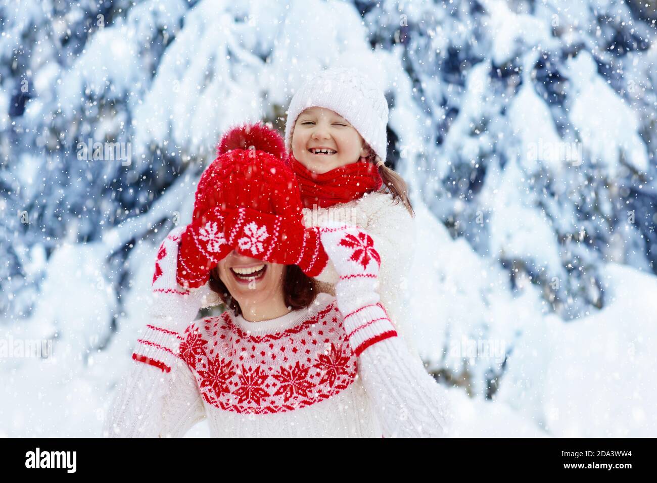 Mutter und Kind in gestrickten Wintermützen spielen im Schnee auf Familienweihnachtsferien. Handgemachte Wollmütze und Schal für Mama und Kind. Stricken für Kinder. Stockfoto