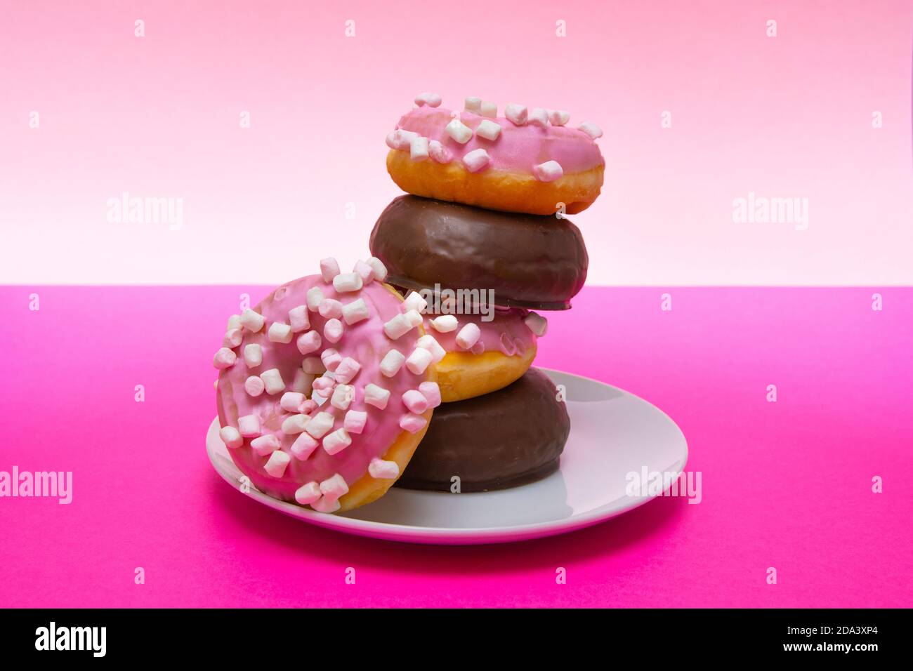 Nahaufnahme eines weißen Tellers rosa Donuts mit Kreuzkümmel und Schokolade bedeckt. Horizontale Fotografie Stockfoto