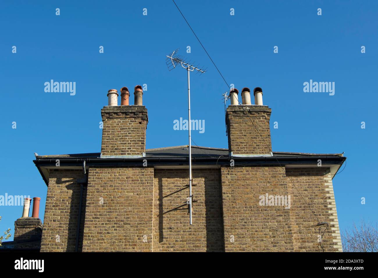 Eine fernsehantenne auf einem hohen Mast ragt zwischen Kaminen über der Ziegelmauer eines Hauses in twickenham, im Südwesten londons, england Stockfoto