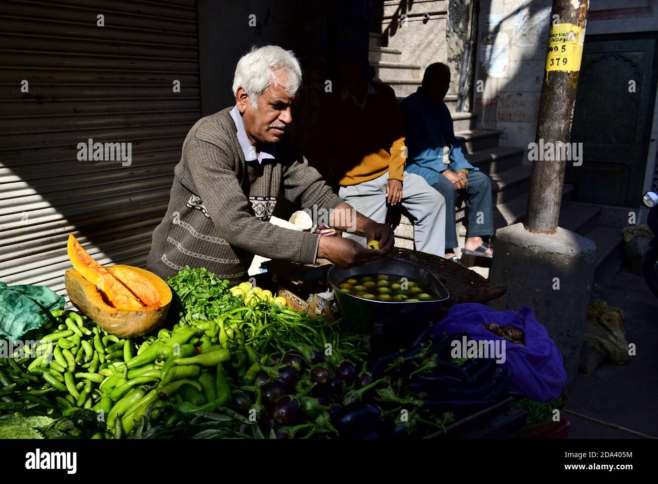 Udaipur, Rajasthan, Indien - Dezember, 2016: Gealterter Verkäufer, der Gemüse auf dem Straßenmarkt verkauft. Indischer Mann Verkäufer in der Nähe von Straßenverkäufer am Morgen Stockfoto