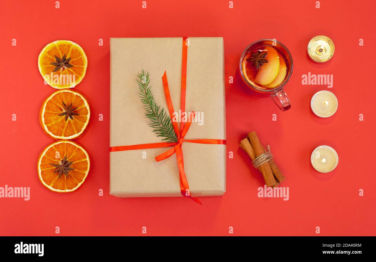 Flach auf rotem Hintergrund mit einem Weihnachtsgeschenk, einer Tasse Glühwein mit Zutaten und Kerzen. Horizontale Ausrichtung, selektiver Fokus, oben Stockfoto