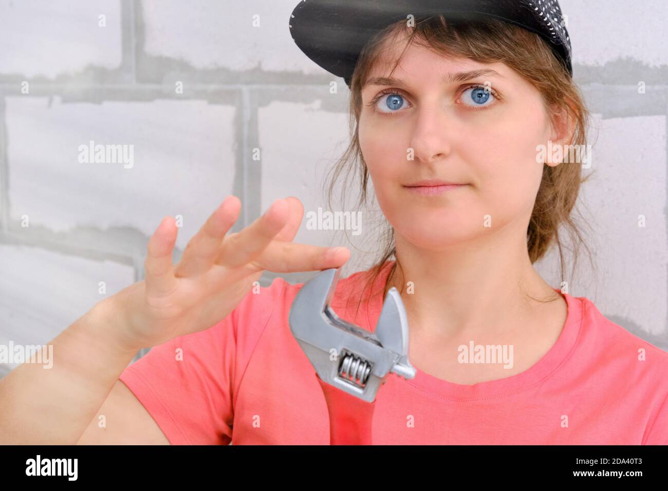 Eine junge Frau in einer Kappe mit einem großen verstellbaren Schraubenschlüssel. Klempner repariert und hält einen roten Schraubenschlüssel. Stockfoto