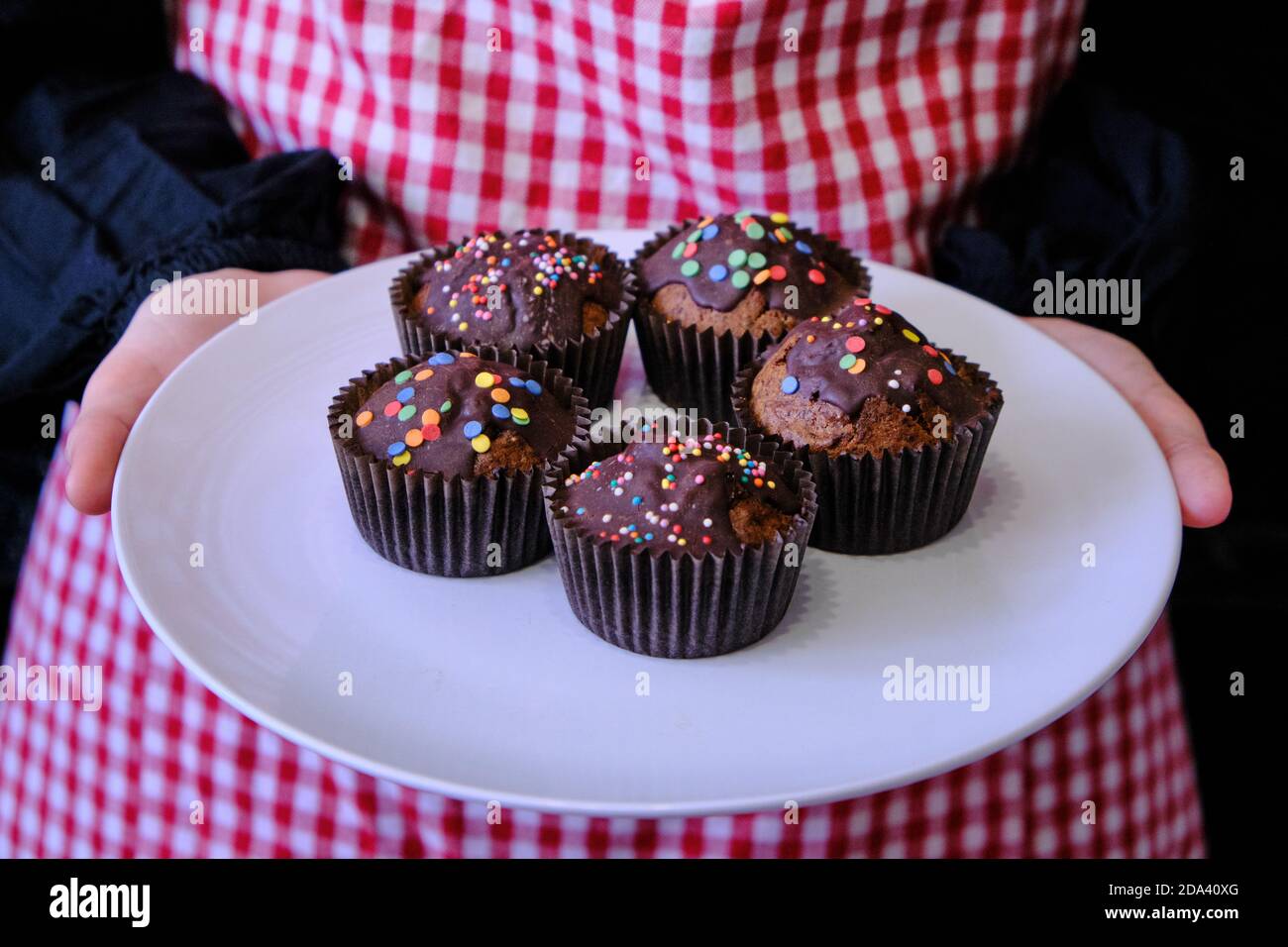 Mädchen hält Muffins mit Schokolade. Frau mit Kuchen in einer Bonbons-Beschichtung.  Teller mit Schokoladenmuffins auf dem Hintergrund eines Mädchens in einer  Schürze Stockfotografie - Alamy