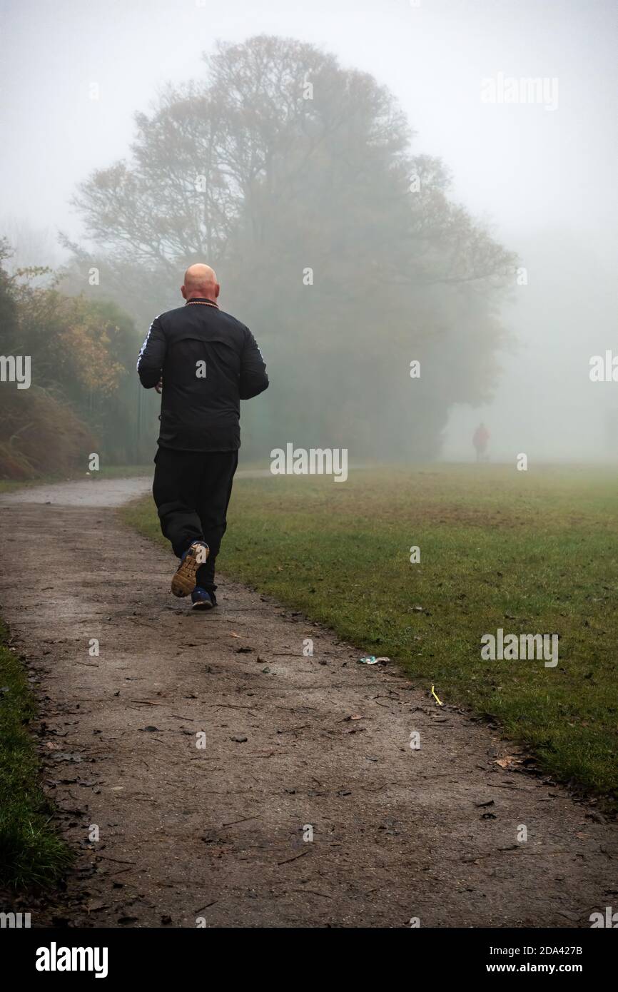 Mann, der in einem öffentlichen Park im Nebel wegläuft Stockfoto