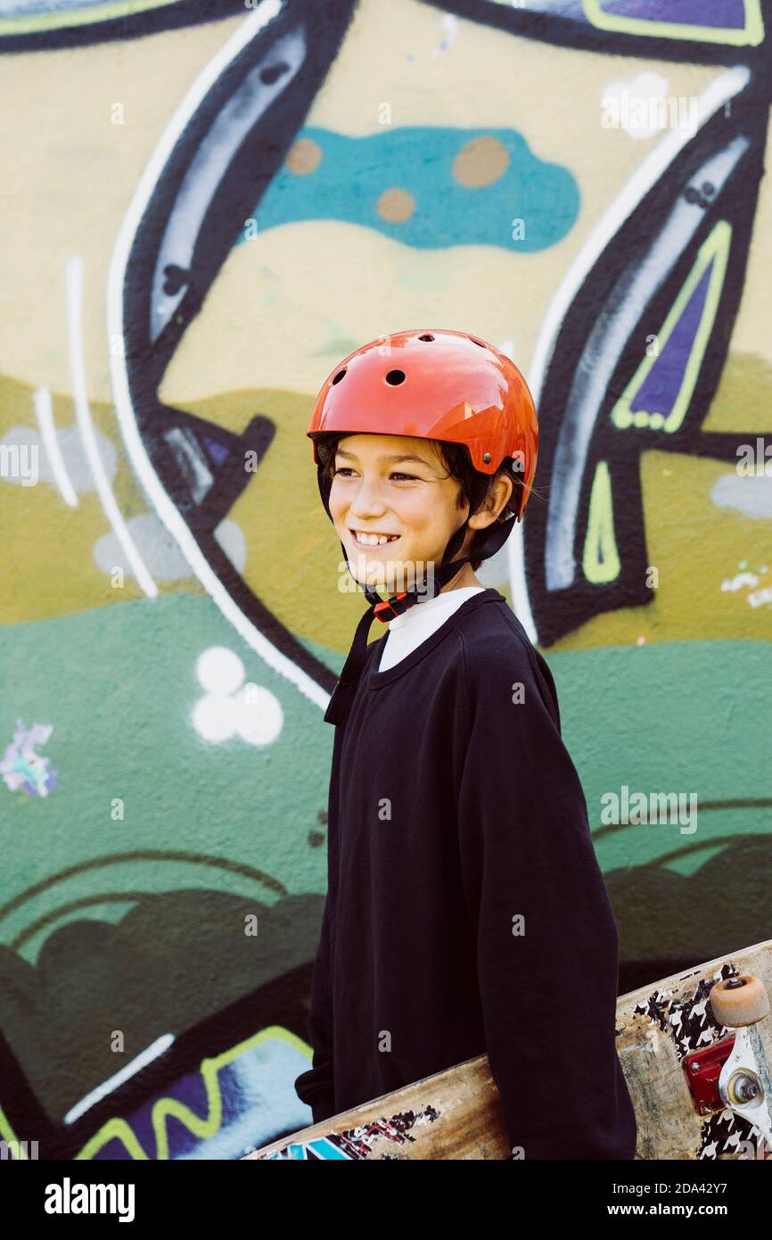 Porträt eines jungen Skater mit einem alten Skateboard Und ein roter Helm vor einem Graffiti-Wandbild Stockfoto