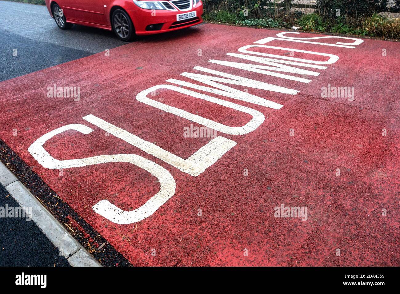 Slow-Schild auf der Straße mit vorbeifahrenden Auto geschrieben Stockfoto