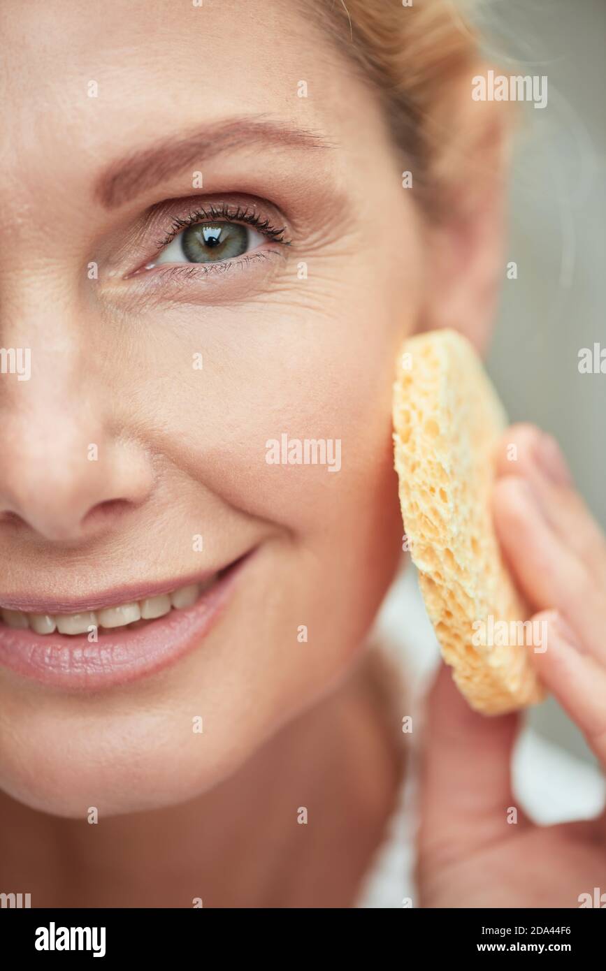 Schöne Frau mittleren Alters kaukasischen mit sauberer glänzender Haut halten Gesichtsschwamm beim Blick auf die Kamera und lächeln. Beauty, Hautpflege und Kosmetologie Konzept Stockfoto