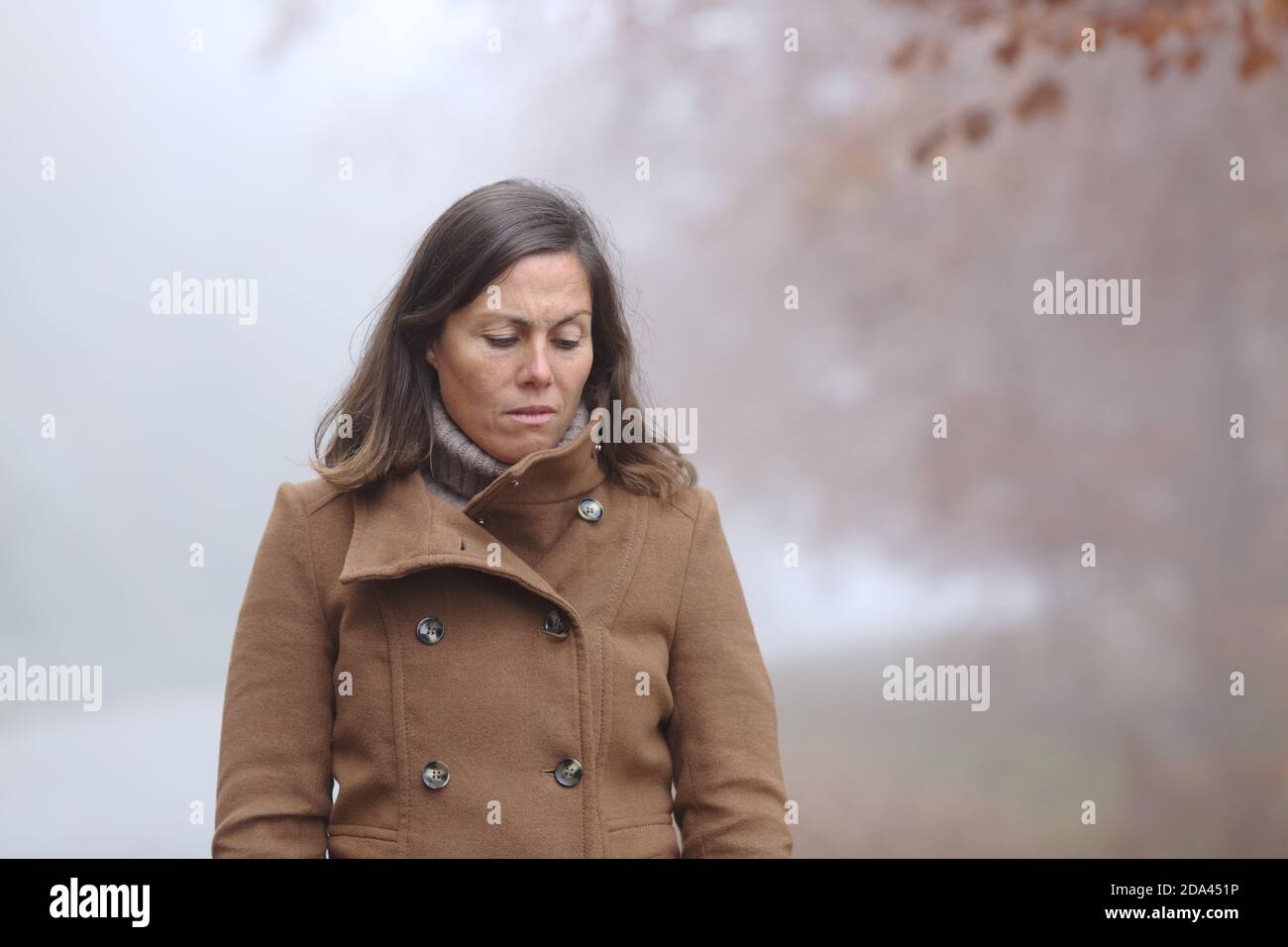 Traurige Frau mittleren Alters, die in einem Wald hinunterschaut Im Herbst ein nebliger Tag Stockfoto