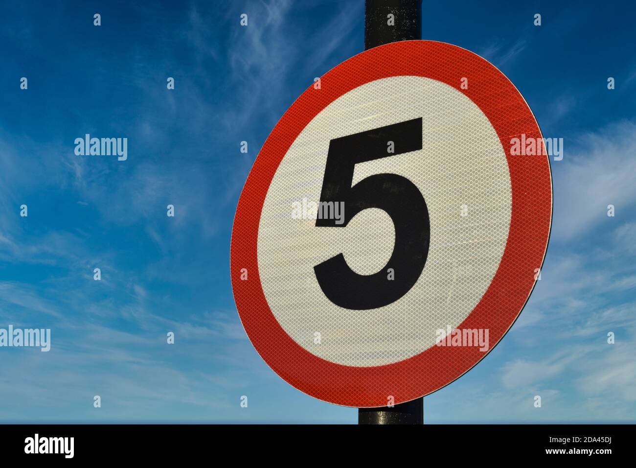 Kreisförmiges 5 Meilen pro Stunde Geschwindigkeitsbegrenzungszeichen mit roter Umrandung, weißem Hintergrund und schwarzer Zahl fünf. Vor blauem Himmel und hellem Wolkenhintergrund. Stockfoto
