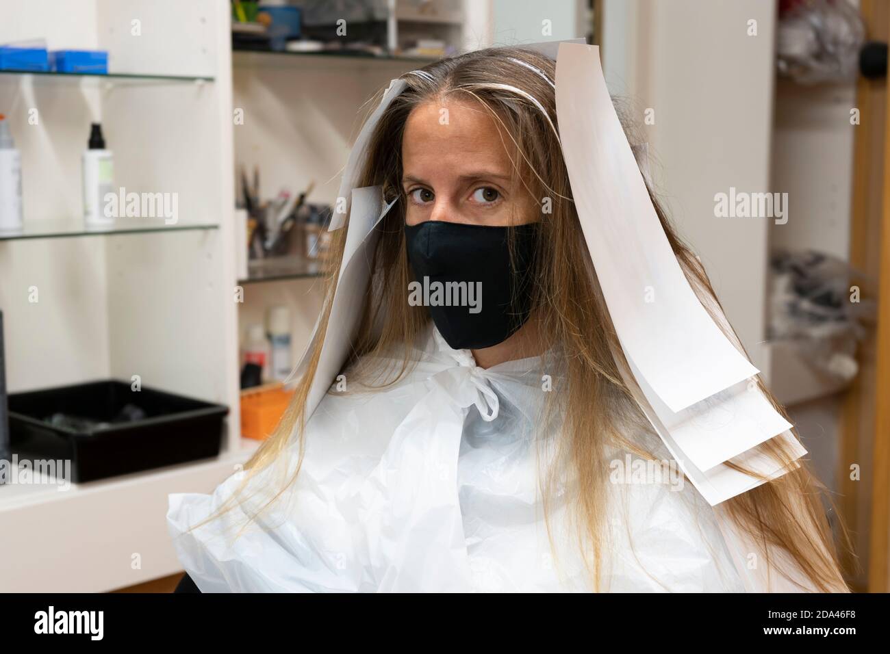 Schöne Frau im Friseursalon, mit Haarfärbepapier oder Aluminiumfolie vor der Änderung der Haarfarbe, trägt medizinische Schutzmaske Gegen coron Stockfoto