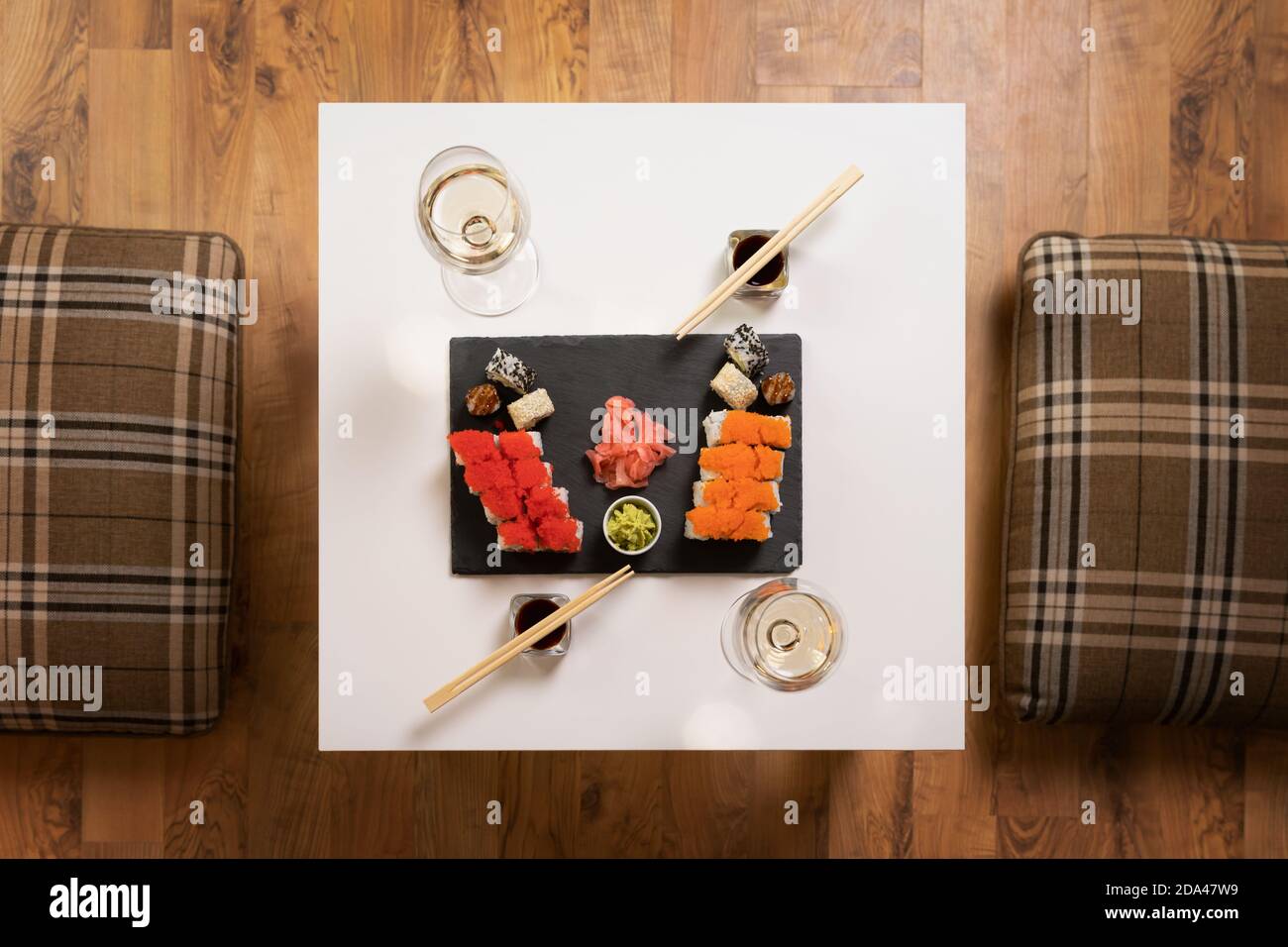 Ein Set aus farbenfrohem Sushi auf einem weißen Tisch mit Wein in einem gemütlichen Raum. Stockfoto