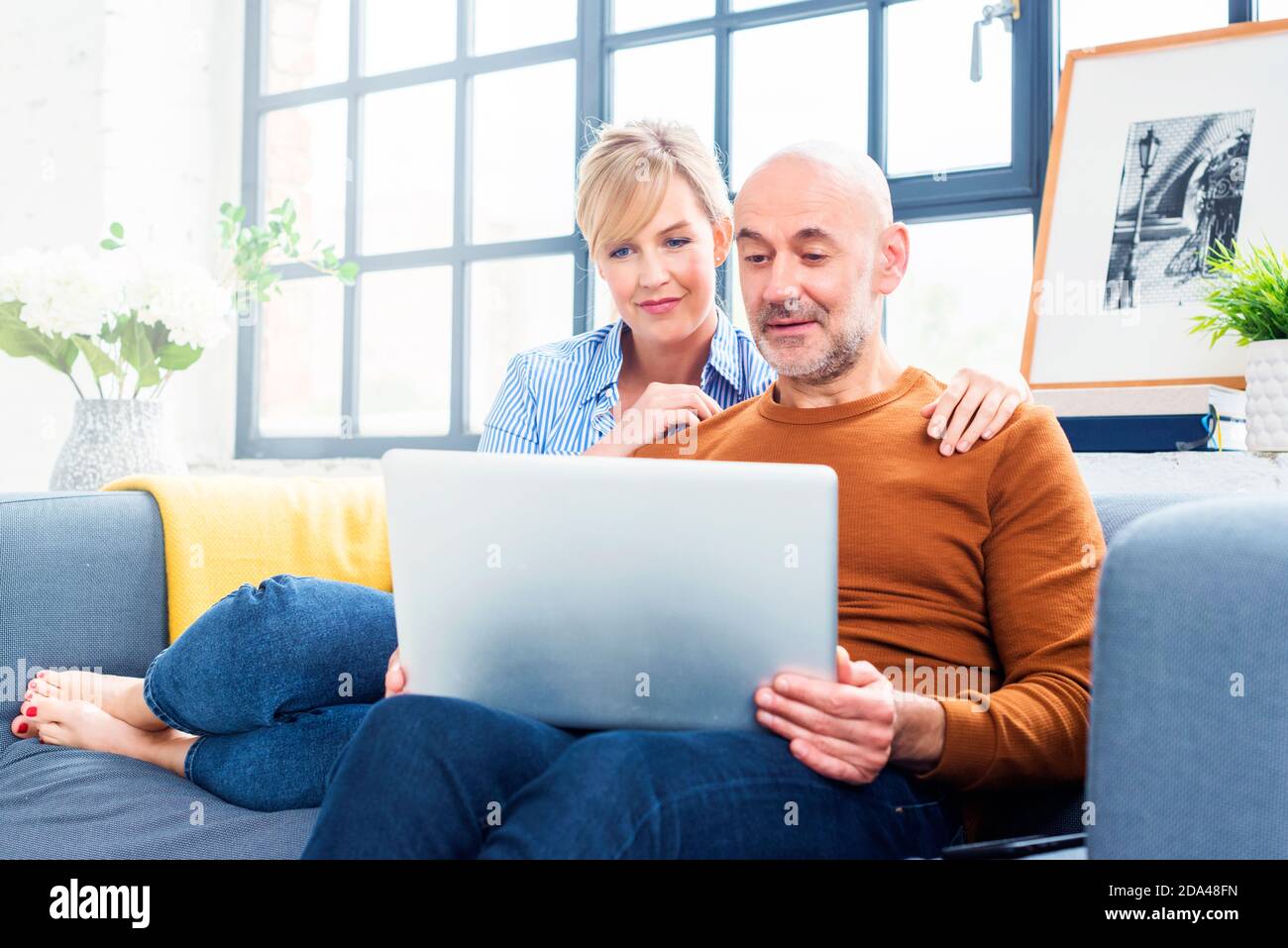 Aufnahme eines glücklichen Paares, das einen Laptop benutzt, während es sich auf dem Sofa zu Hause entspannt. Stockfoto
