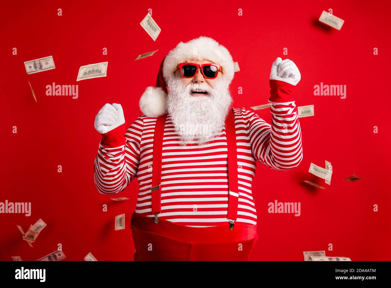 Foto von Rentner Großvater grauen Bart heben Fäuste riesige Last Geld tragen weihnachtsmann Kostüm Hosenträger Sonnenschutzhandschuhe gestreiftes Hemd Kappe isoliert rot Stockfoto