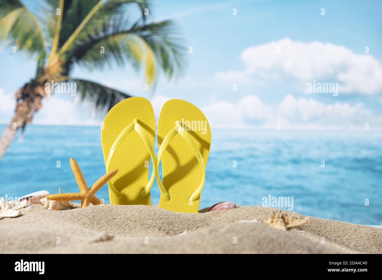 Ein Paar gelbe Pantoffeln in den Sand mit Seesternen gelegt Auf dem Meer und Palmen Hintergrund Stockfoto