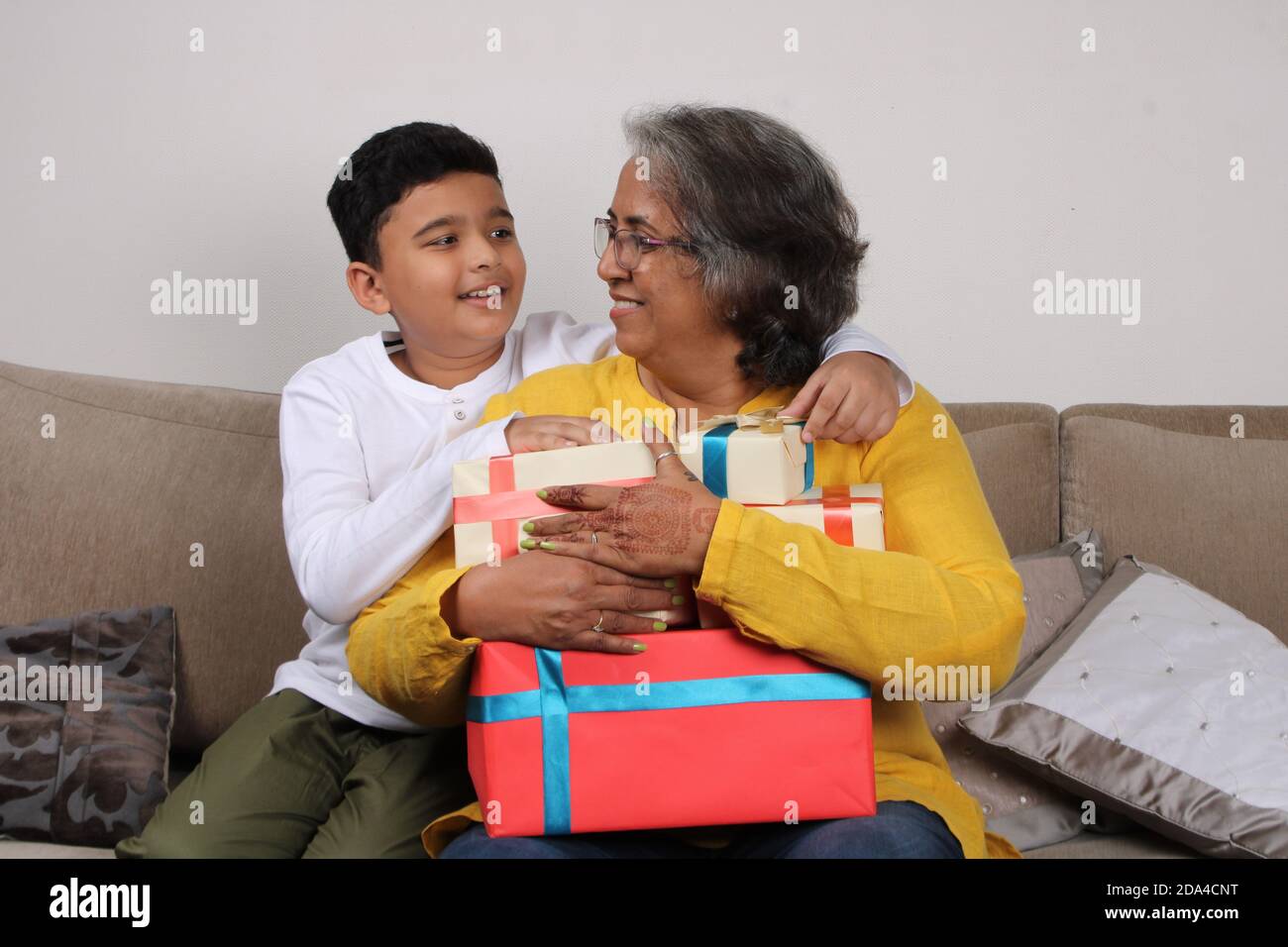 Fröhliches indisches Kind und seine Enkelmutter sitzen auf dem Sofa mit Geschenken. Stockfoto