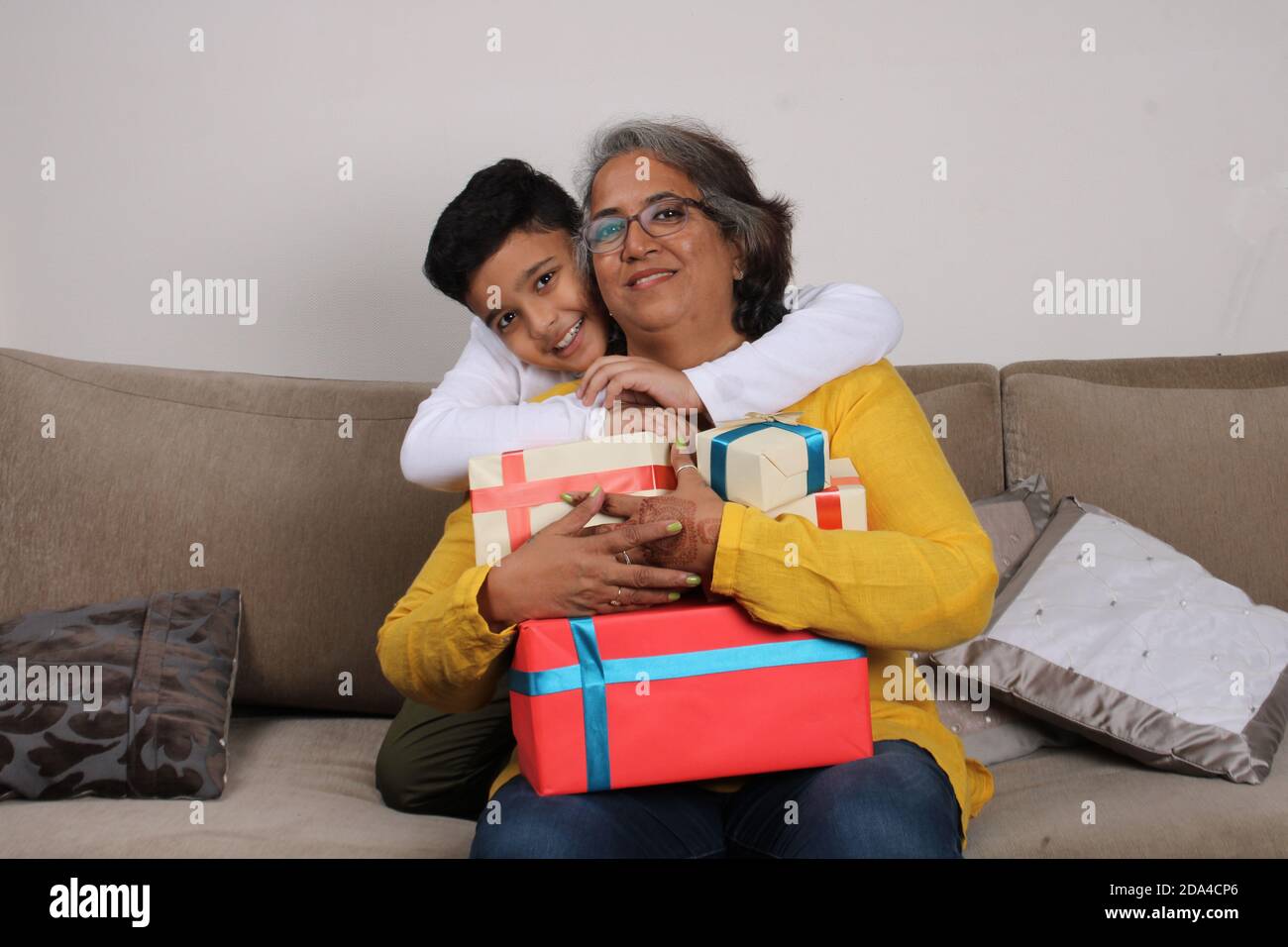 Fröhliches indisches Kind und seine Enkelmutter sitzen auf dem Sofa mit Geschenken. Stockfoto