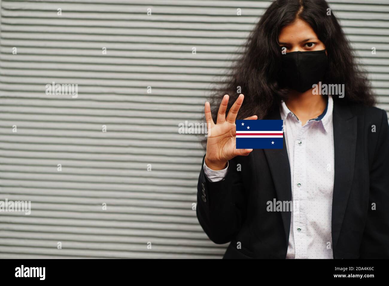 Asiatische Frau bei formeller Kleidung und schwarz schützen Gesichtsmaske halten Howland und Baker Islands Flagge bei der Hand vor grauem Hintergrund. Coronavirus bei Country con Stockfoto