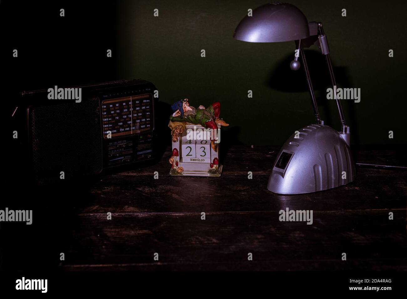 Nahaufnahme eines Vintage-Kalenders mit einer Lampe und einem Radio auf dem Tisch vor dunklem Hintergrund Stockfoto