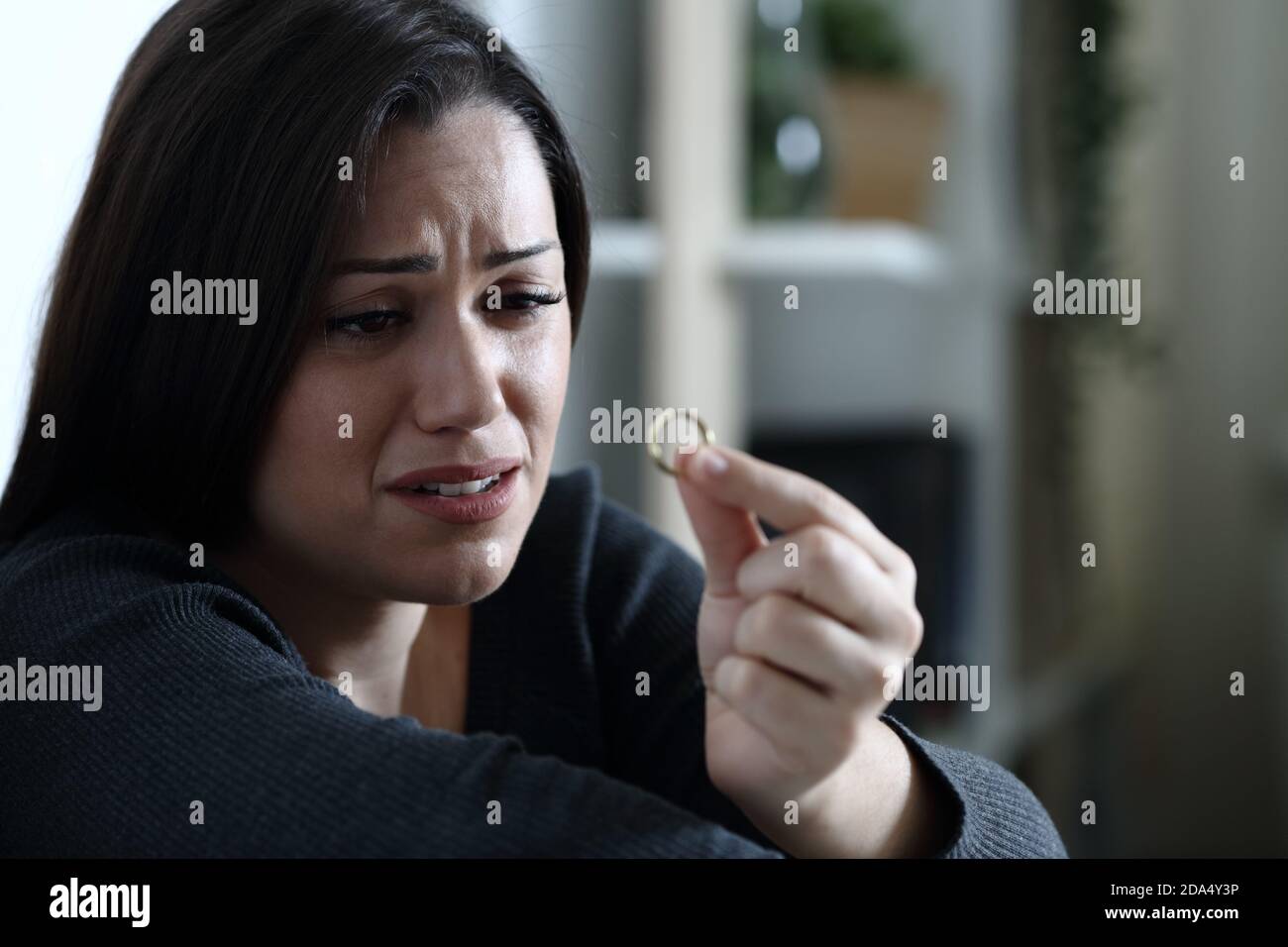 Traurige Frau schaut auf Ehering beschwert sich allein denkend in Scheidung in der dunklen Nacht zu Hause Stockfoto